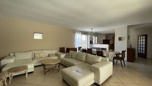 Un salón amplio con un sofá grande en forma de L, una pequeña mesa redonda y una zona de comedor con mesa y sillas.