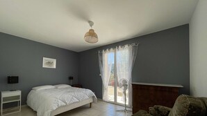 Un dormitorio con cama, mesita de noche, silla, ventana con cortinas y ventilador de techo.