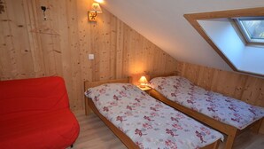 A room with wooden walls and a sloped ceiling, featuring two wooden beds with floral bedding, a red sofa, and a skylight. - Charming Apartment in Les Gets Center, 150m from Chavannes Slopes (Les Gets)