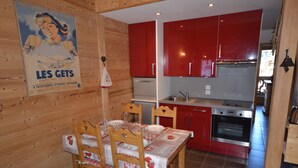 A wooden interior with a dining table set for four, red kitchen cabinets, and a poster on the wall. - Charming Apartment in Les Gets Center, 150m from Chavannes Slopes (Les Gets)