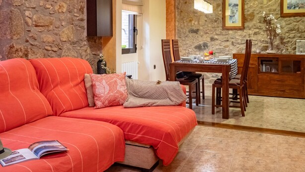 A cozy living room with a red sofa, a dining table with chairs, and a stone wall. - Charming Rustic-Modern House with A/C & WiFi, 200m from Beach in Palamós Center (Palamós)