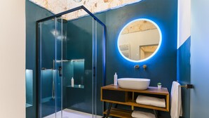 A modern bathroom with a glass-enclosed shower, a round mirror with a light, and a wooden vanity with a white sink.
