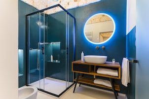 A modern bathroom with a glass-enclosed shower, a round mirror with a light, and a wooden vanity with a white sink.