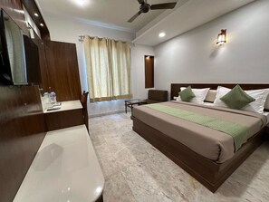 A hotel room with a large bed, a desk, a chair, a vanity, and a ceiling fan. - Svaruchi (A Boutique Hotel) (New Delhi)