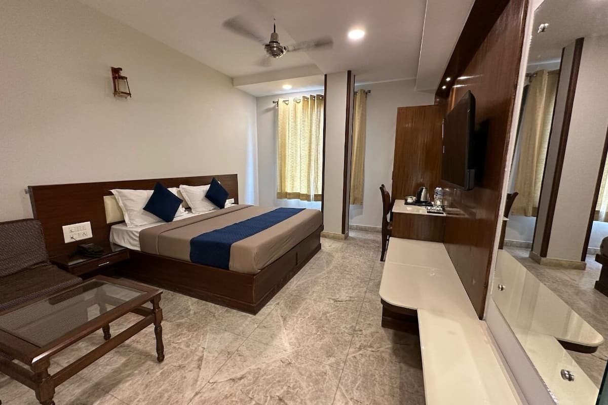 Une chambre d’hôtel comprenant un lit, une table à plateau en verre, un banc en bois, une coiffeuse avec un miroir et un ventilateur de plafond.