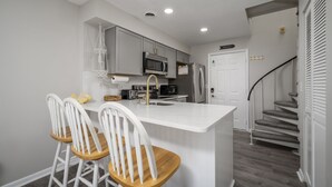 A modern kitchen with a central island, white bar stools, and a staircase leading to a second floor. - New Listing!  Updated 1 bedroom bayside with a pool! (Ocean City)
