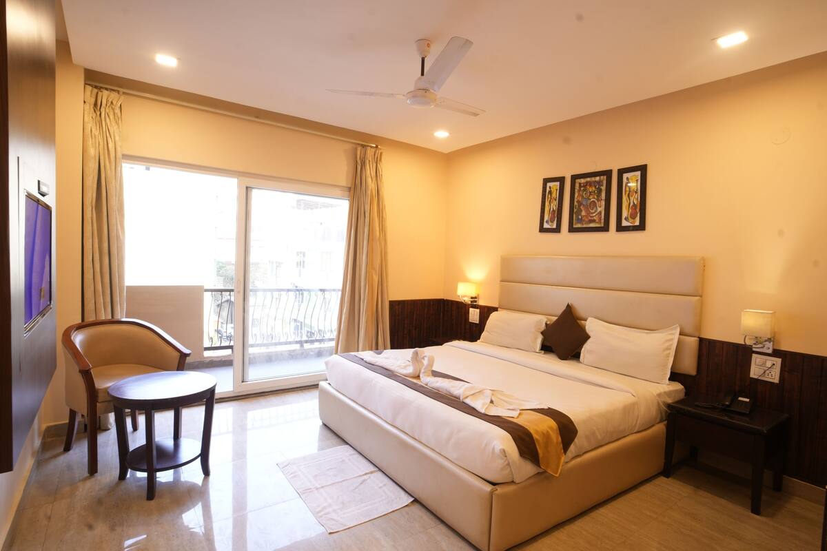 A hotel room with a bed, a chair, a desk, a ceiling fan, and a balcony with curtains.