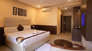 A hotel room with a large bed, a ceiling fan, an air conditioning unit, a TV, and a wooden desk. - Hotel Royale Hills (Narendranagar)