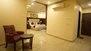 A hotel room with a bed, a chair, a small table, and an air conditioning unit on the wall. - Hotel Royale Hills (Narendranagar)