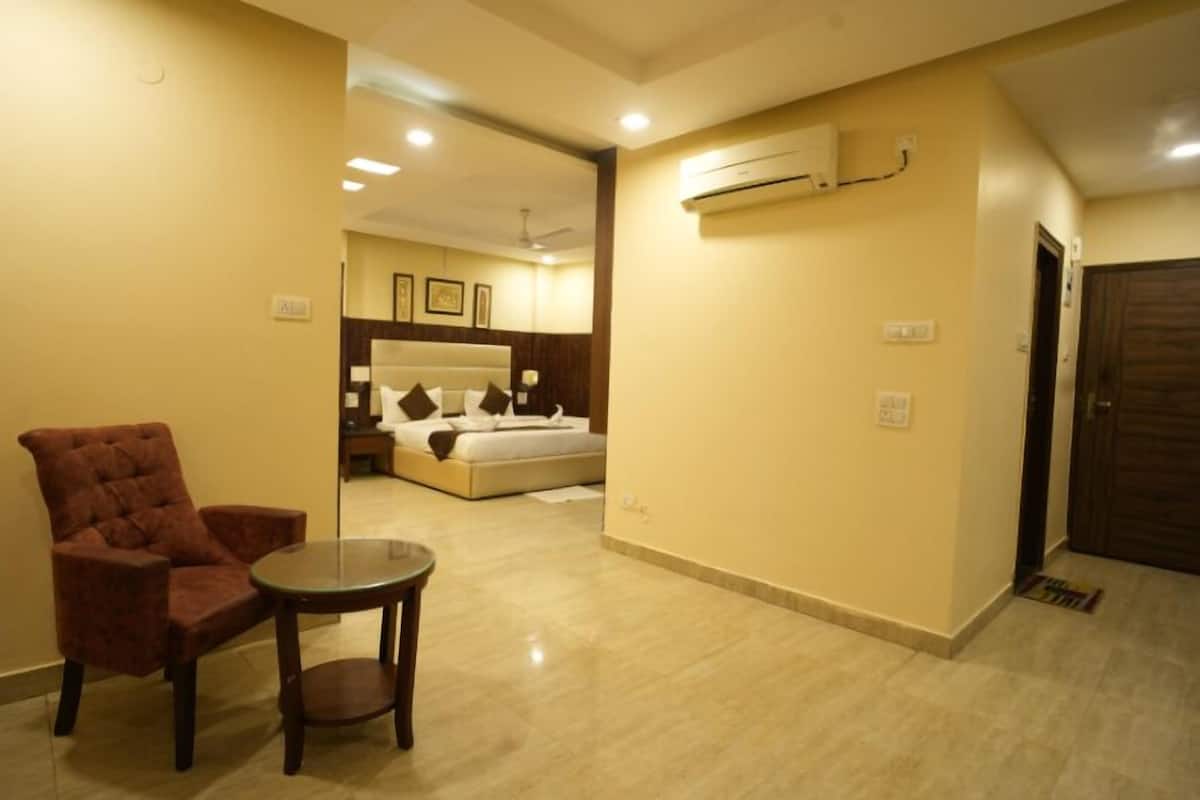 A hotel room with a bed, a chair, a small table, and an air conditioning unit on the wall.