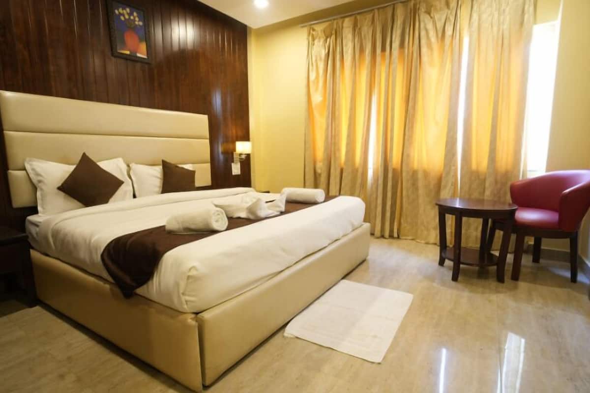 A hotel room with a large bed, a small table, a red chair, and a window with curtains.