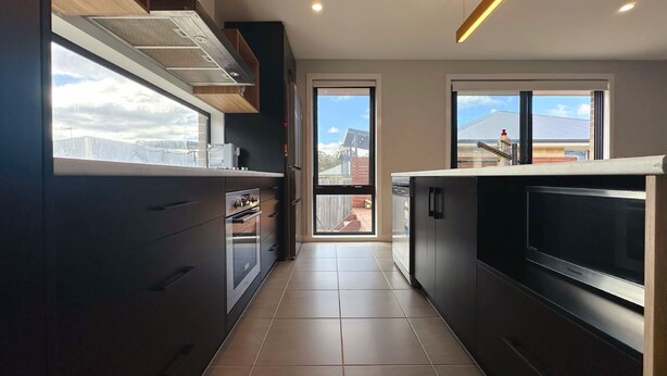 Una cocina moderna con armarios oscuros, horno empotrado y un ventanal grande.