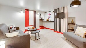 A modern living room with a grey sofa, a round coffee table, and a kitchen area with a red accent wall. - 229 Suite Fantasyland - Superb apartment (Paris 02 Bourse)