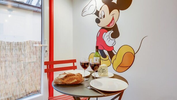 A table with a Mickey Mouse mural, a loaf of bread, two glasses of red wine, and a bottle of champagne. - 229 Suite Fantasyland - Superb apartment (Paris 02 Bourse)