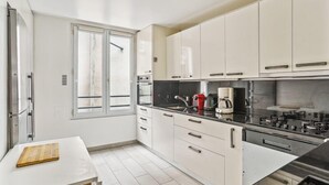 A modern kitchen with white cabinets, a black countertop, and stainless steel appliances. - 618 Suite Elisabeth - Stunning Apartment in Paris (Paris 10 Entrepôt)