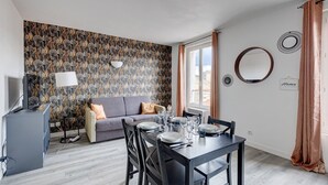 Een moderne woonkamer met een grijze bank, een eettafel gedekt voor vier personen en behang met een patroon.