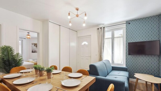 A modern living room with a dining table set for four, a blue sofa, and a TV mounted on the wall. - 864 Suite Iris - Superb apartment (Montreuil)