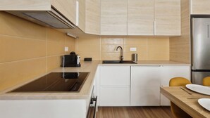 A modern kitchen with a black induction cooktop, a stainless steel refrigerator, and white cabinetry. - 864 Suite Iris - Superb apartment (Montreuil)