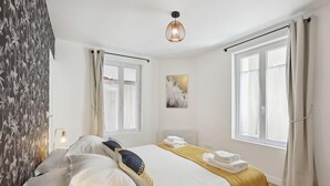 A hotel room with a bed, a bedside table, a lamp, a window with curtains, and a wall-mounted artwork. - 864 Suite Iris - Superb apartment (Montreuil)