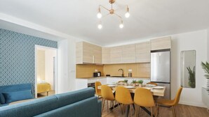 A modern kitchen with wooden cabinets, a dining table with yellow chairs, and a blue sofa in the living area. - 864 Suite Iris - Superb apartment (Montreuil)