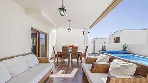 Une terrasse ensoleillée, meublée de meubles en osier, avec une table à manger et une piscine.
