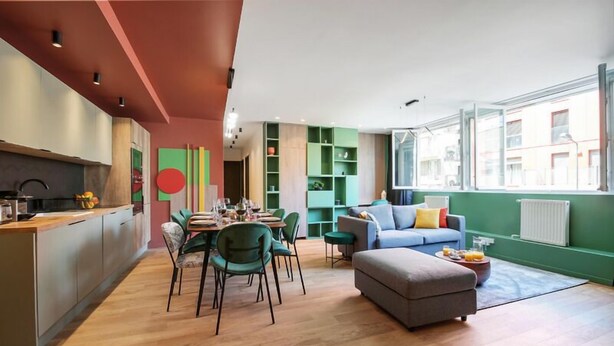 A modern apartment with a kitchen, dining area, and living room. It features a large window, green shelving, and a grey sofa. - 221 Suite Juju - Superb Apartment in Paris (Paris 13 Gobelins)