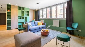 A modern living room with a blue sofa, green shelving, a coffee table with drinks, and a view through large windows. - 221 Suite Juju - Superb Apartment in Paris (Paris 13 Gobelins)
