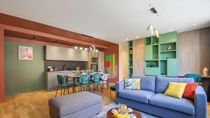 A modern living room with a sofa, ottoman, and coffee table. There is a dining area with chairs and a table. The room has a kitchen with cabinets and a countertop. - 221 Suite Juju - Superb Apartment in Paris (Paris 13 Gobelins)