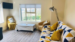 A living room with a sofa, two armchairs, a coffee table, and a TV mounted on the wall. - Brand new 2 Bedroom Home Overlooking Kenmare Bay Estuary (Kenmare)