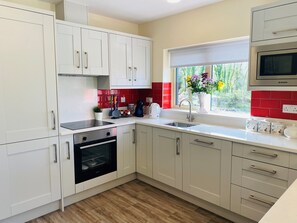 Una cocina moderna con armarios blancos, horno empotrado, pileta de acero inoxidable y ventana con vista a follaje.