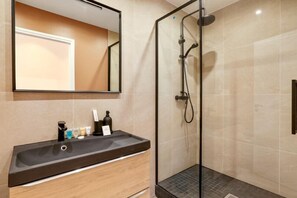 Een moderne badkamer met een douchecabine van glas, een wastafelmeubel met een donker aanrechtblad en een spiegel boven de wastafel.