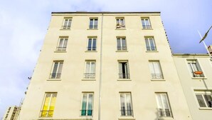 Un immeuble à plusieurs étages doté d’une façade symétrique, avec des fenêtres et des balcons régulièrement espacés.