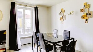 Un espace repas moderne avec une table et des chaises noires, une œuvre d’art murale aux motifs géométriques et une fenêtre agrémentée d’un rideau noir.