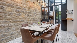 A dining area with a stone wall, a modern chandelier, and a view through large windows. - 334 Parisian Loft - Superb Apartment in Paris (Paris 10 Entrepôt)