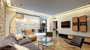 A modern living room with a stone wall, a glass coffee table, leather sofas, and a mounted TV. - 334 Parisian Loft - Superb Apartment in Paris (Paris 10 Entrepôt)