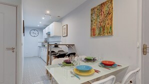 A dining area with a table set for four, a clock on the wall, and a colorful abstract painting above the table. - 234 Office New York - Apartment in Paris (Paris 20 Ménilmontant)