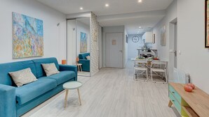 A modern living room with a blue sofa, a small round table, and a dining area with a white table and chairs. - 234 Office New York - Apartment in Paris (Paris 20 Ménilmontant)