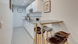 A modern kitchen with a dining area, featuring a clock, a microwave, and a sink. - 234 Office New York - Apartment in Paris (Paris 20 Ménilmontant)