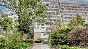 A modern apartment building with a stone pathway leading to the entrance, surrounded by lush greenery and flowering plants. - 234 Office New York - Apartment in Paris (Paris 20 Ménilmontant)