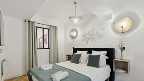 A modern bedroom with a large bed, a bedside table, a wall-mounted light, and a decorative wall piece. - 266 Suite Montefiore Superb apartment in Paris. (Paris 02 Bourse)