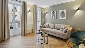 A modern living room with a sofa, two side tables, and artwork on the wall. - 266 Suite Montefiore Superb apartment in Paris. (Paris 02 Bourse)