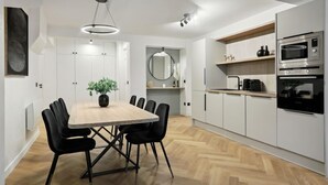 A modern kitchen with white cabinets, a wooden dining table, black chairs, and built-in appliances. - 266 Suite Montefiore Superb apartment in Paris. (Paris 02 Bourse)