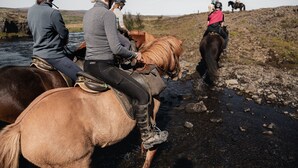 Eine Gruppe von Menschen reitet Pferde entlang eines felsigen Flussufers.