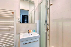 A modern bathroom with a glass-enclosed shower, a white sink with toiletries, and a mirror above the sink. - 251 Suite Foy - Superb apartment in Paris (Paris 02 Bourse)