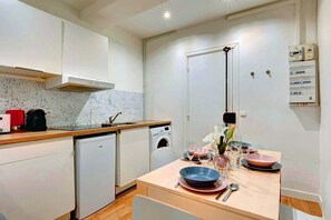 A compact kitchen with a washing machine, a coffee maker, and a dining table set with plates and glasses. - 251 Suite Foy - Superb apartment in Paris (Paris 02 Bourse)