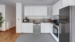 A modern kitchen with white cabinets, a stainless steel refrigerator, a dishwasher, and a built-in oven. - 340 Suite Emile - Superb apartment (Clichy)