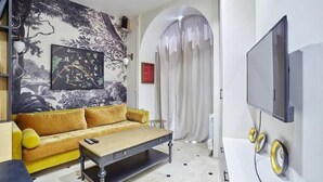 Un salon moderne avec un canapé jaune, une table basse, un grand téléviseur et une fresque murale.