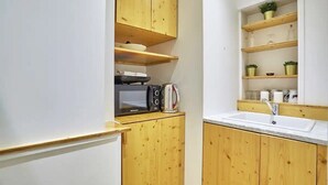 Una cocina compacta con armarios de madera, un microondas, una tetera y un lavabo.