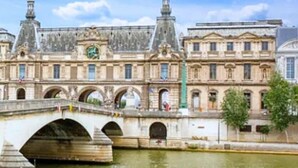 Un edificio histórico con un puente sobre un río, que presenta arquitectura clásica y una torre de reloj.