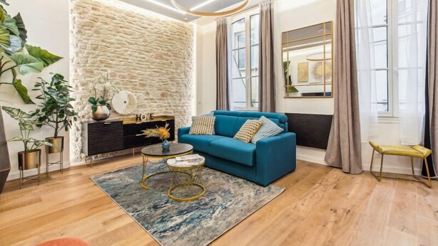 Un salon moderne avec un canapé bleu, un mur décoratif en pierre et une grande fenêtre agrémentée de rideaux.